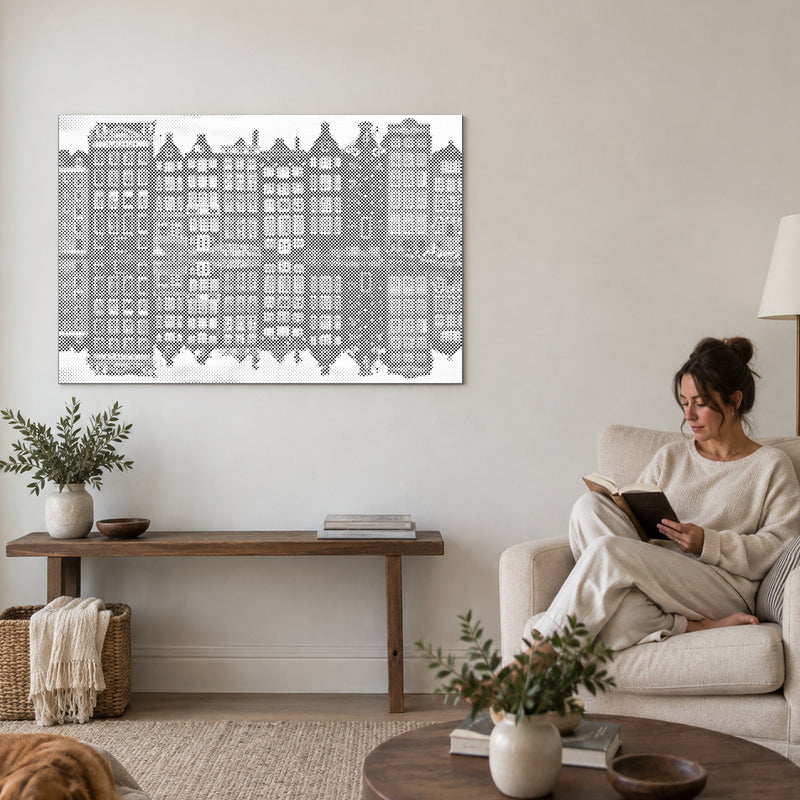 Stippenschilderij “Amsterdamse Huizen”, aan een muur in de woonkamer, met iemand die ernaast in een fauteuil leest.