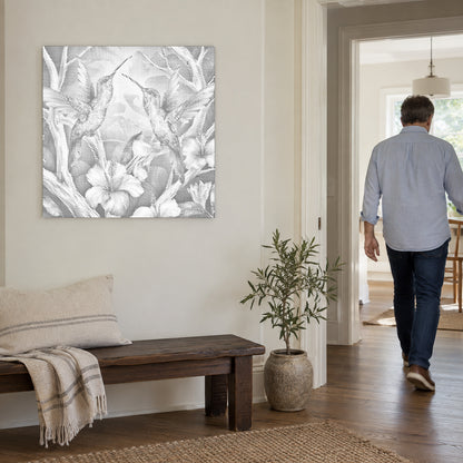 Stippenschilderij “Kolibries tussen bloemen”, aan een lichte muur, met iemand die door de deur ernaast loopt.